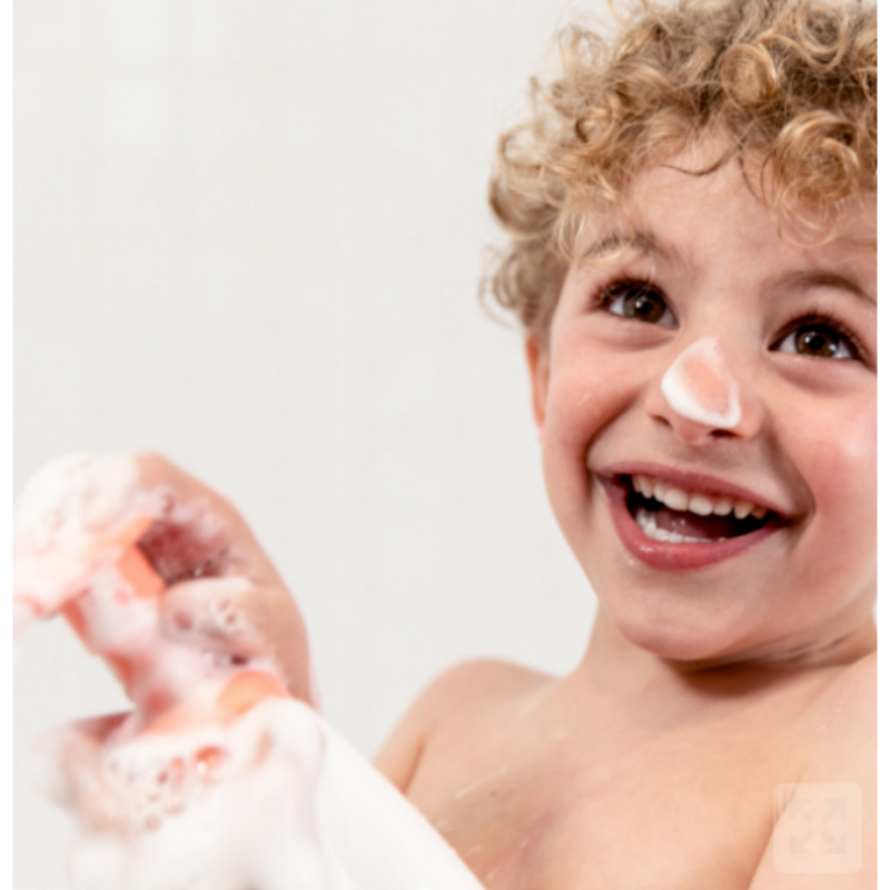 mousse detergente per bambini bianca e arancio con bimbo biondo che sorride e ne ha un pò sul naso