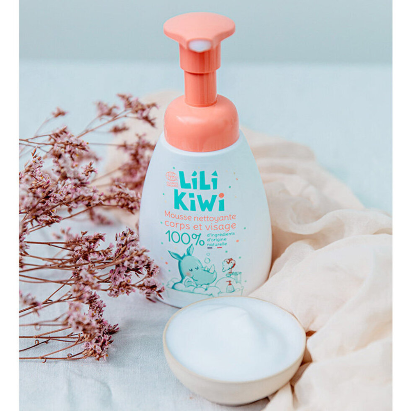 mousse detergente per bambini bianca e arancio appoggiata su una mussola color beige e fiori secchi