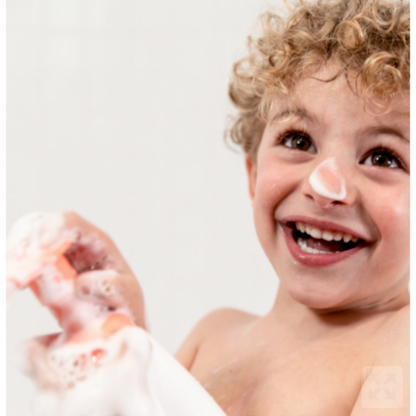 mousse detergente per bambini bianca e arancio con bimbo biondo che sorride e ne ha un pò sul naso