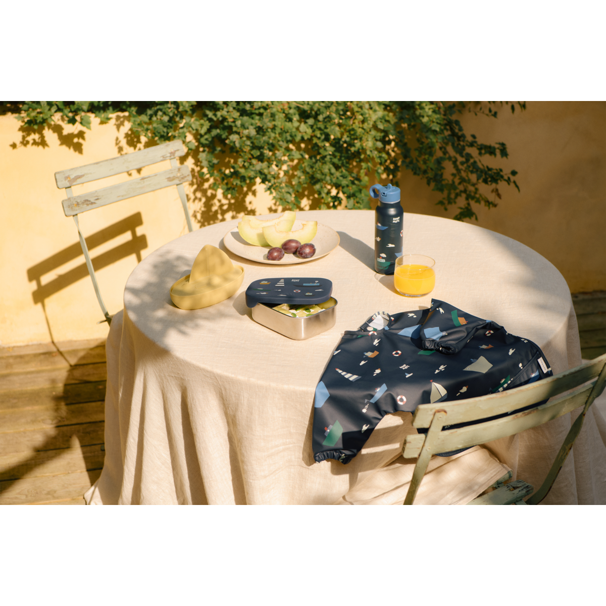 tavola apparecchiata all'aperto con lunchbox blu e borraccia e bavaglio liewood