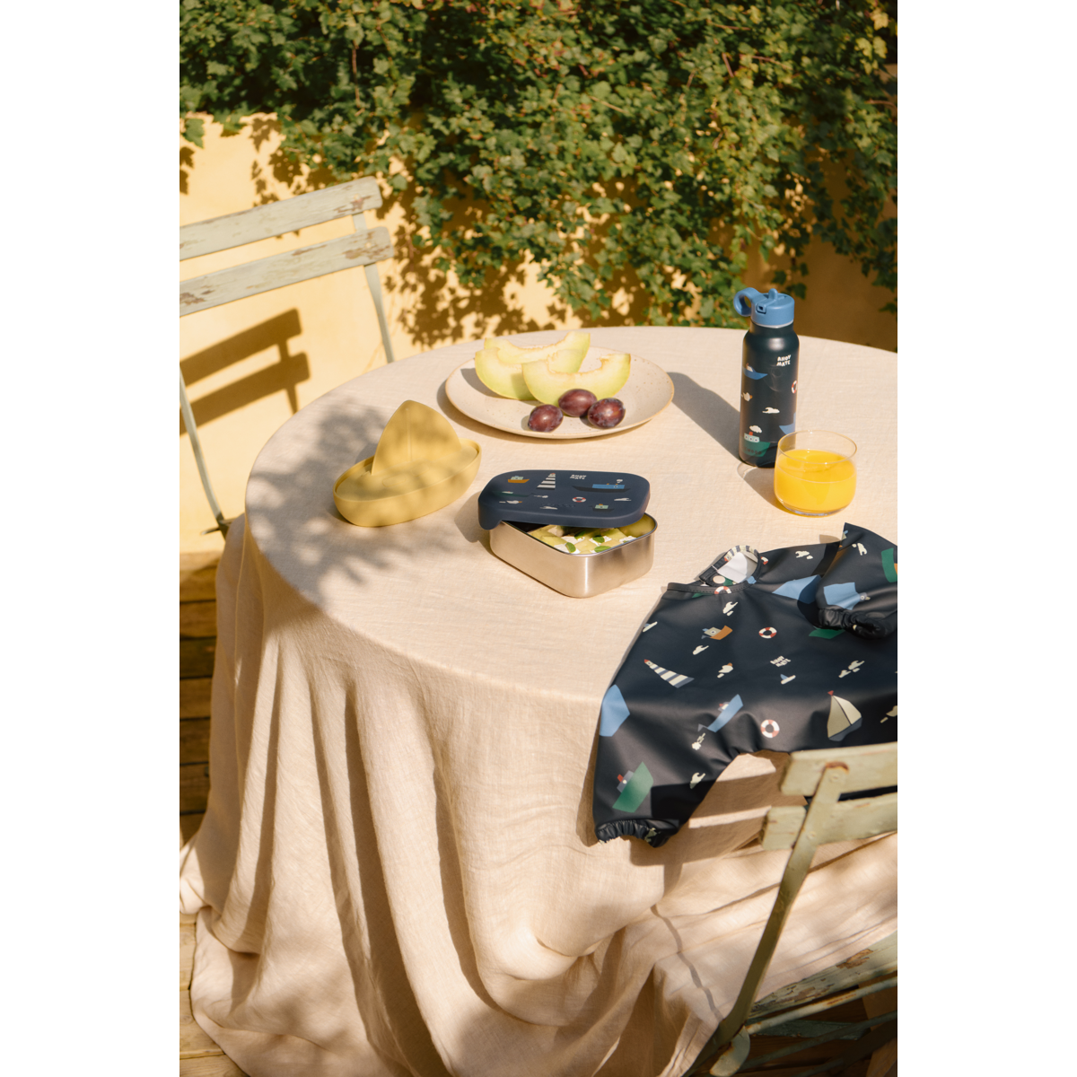 tavola apparecchiata all'aperto con lunchbox blu e borraccia e bavaglio liewood